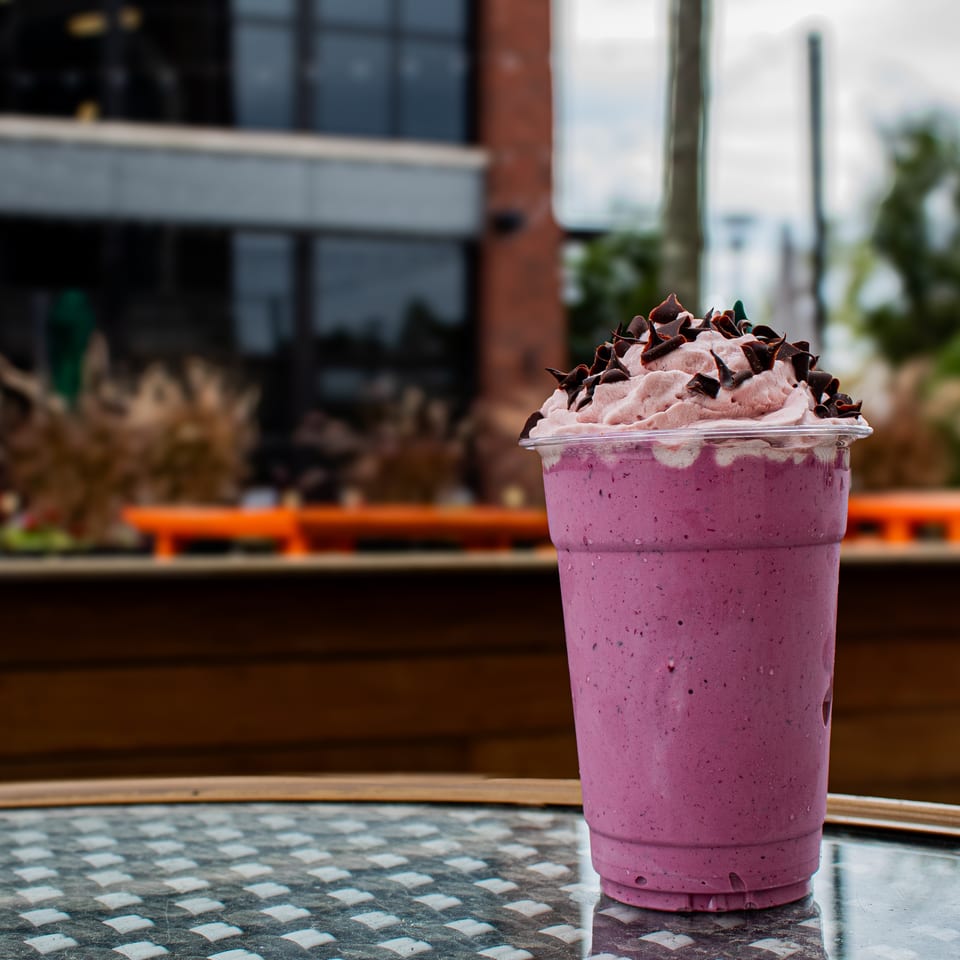 Purple berry smoothie topped with pink whipped cream and chocolate shavings on a café patio table.