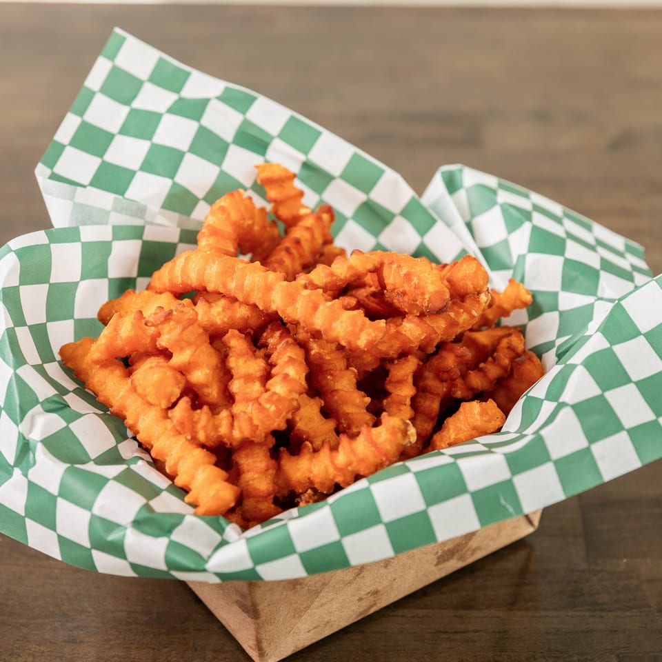 Basket of golden crinkle-cut fries served in green-and-white checkered paper on a wooden table.