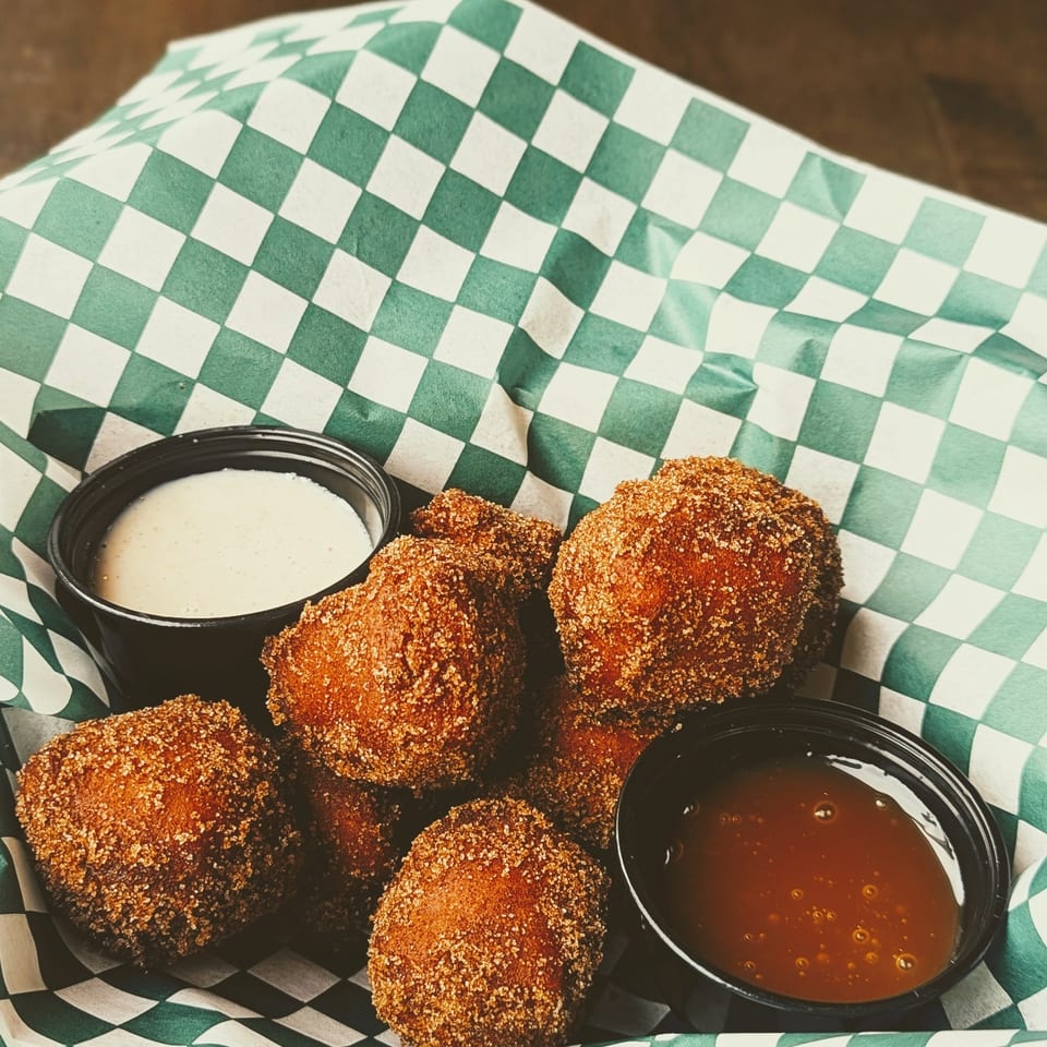 Crispy breaded bites served with creamy white and reddish dipping sauces on green-and-white checkered paper.