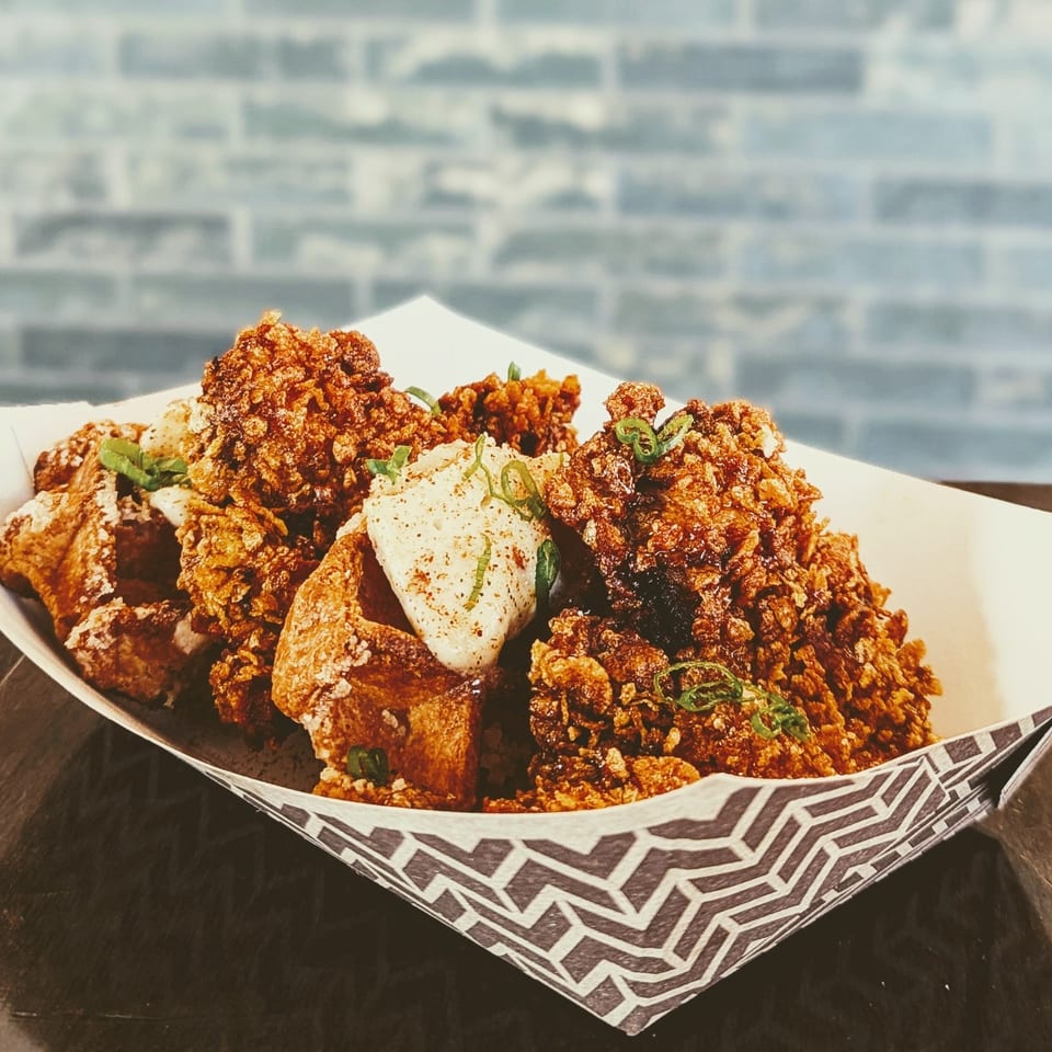 Crispy fried chicken pieces and seasoned potato wedges topped with green onions, served in a patterned paper-lined basket.