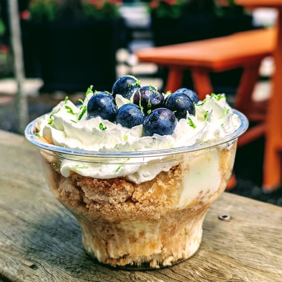 Layered blueberry dessert with whipped cream and lime zest in a glass, served on a rustic wooden table.