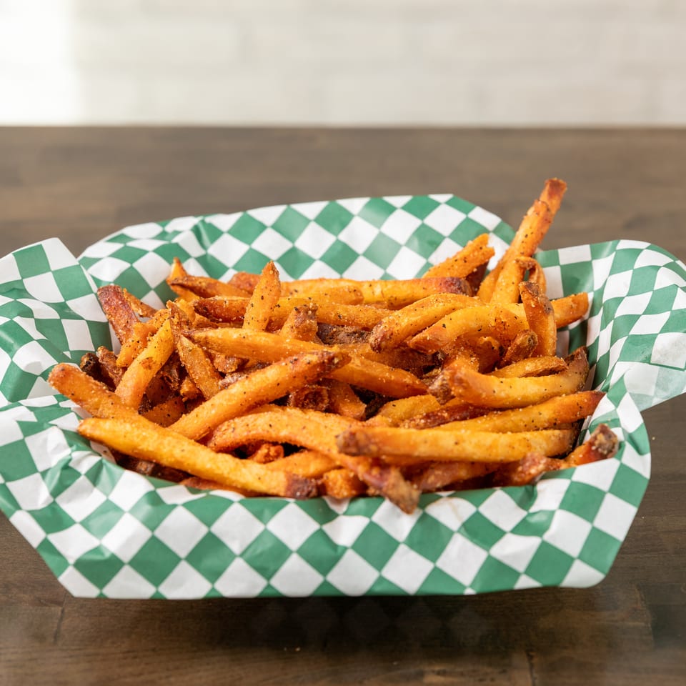 Seasoned golden fries piled in a tray lined with green-and-white checkered paper on a wooden table.